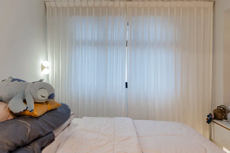 Bed dressed beside full height curtains